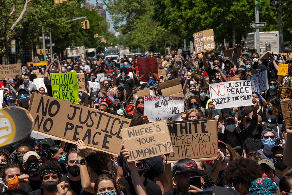 A big crowd of people gathers in Harlem to protest the death of George Floyd. Many signs say "No Justice No Peace."