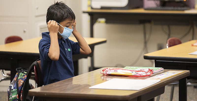 Second grader Ernesto Beltran Pastrana puts on his face mask while attending class during the first day of partial in-person instruction at Garfield Elementary School in Oakland, Calif.