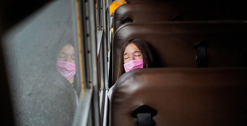 A female student wearing a pink mask sleeps on a school bus.
