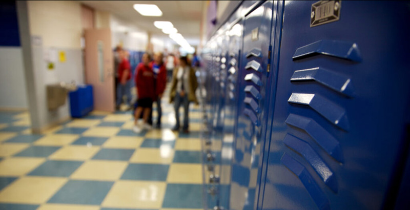 A photo of a school hallway with blue lockers and checkered tile flooring