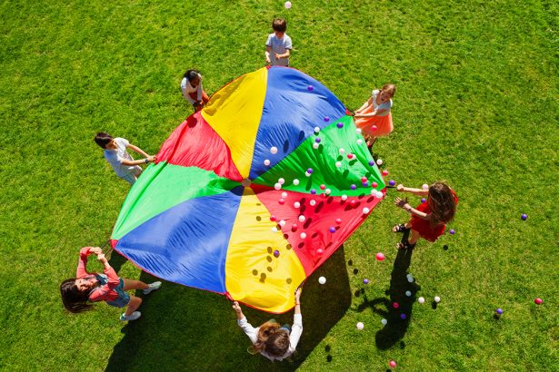 Happy kids waving rainbow parachute full of balls