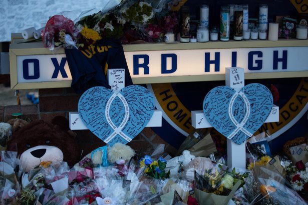 A memorial outside of Oxford High school includes flowers, candles blue heart cutouts with writing on them and stuffed animals