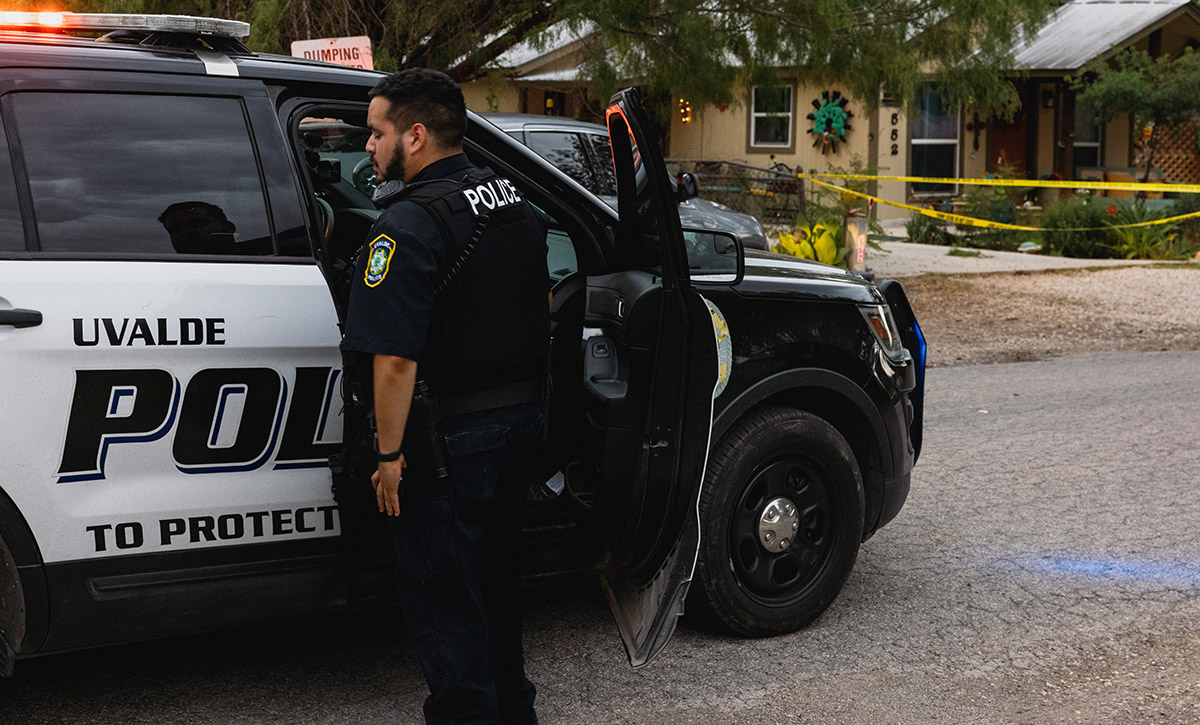 A Uvalde police officer stands near an open police car door.