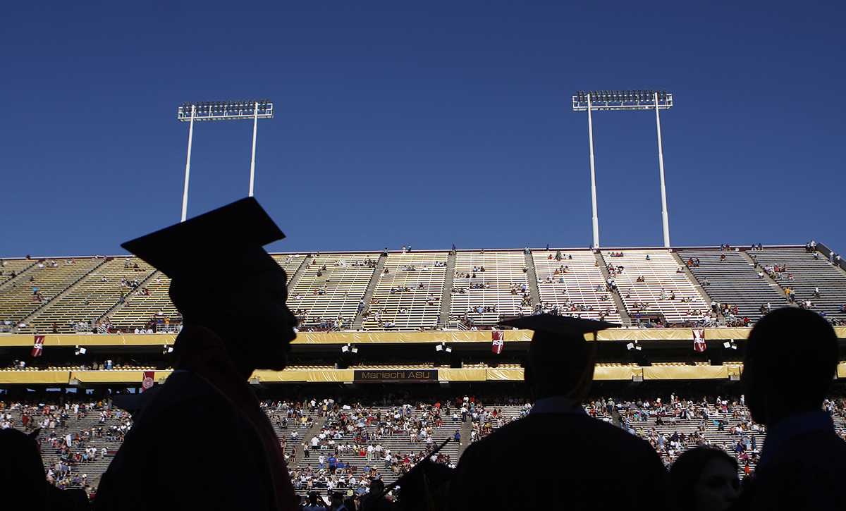 Students wearing graduation caps are seen in silhouette against a full stadium at Sun Devil Stadium in Arizona