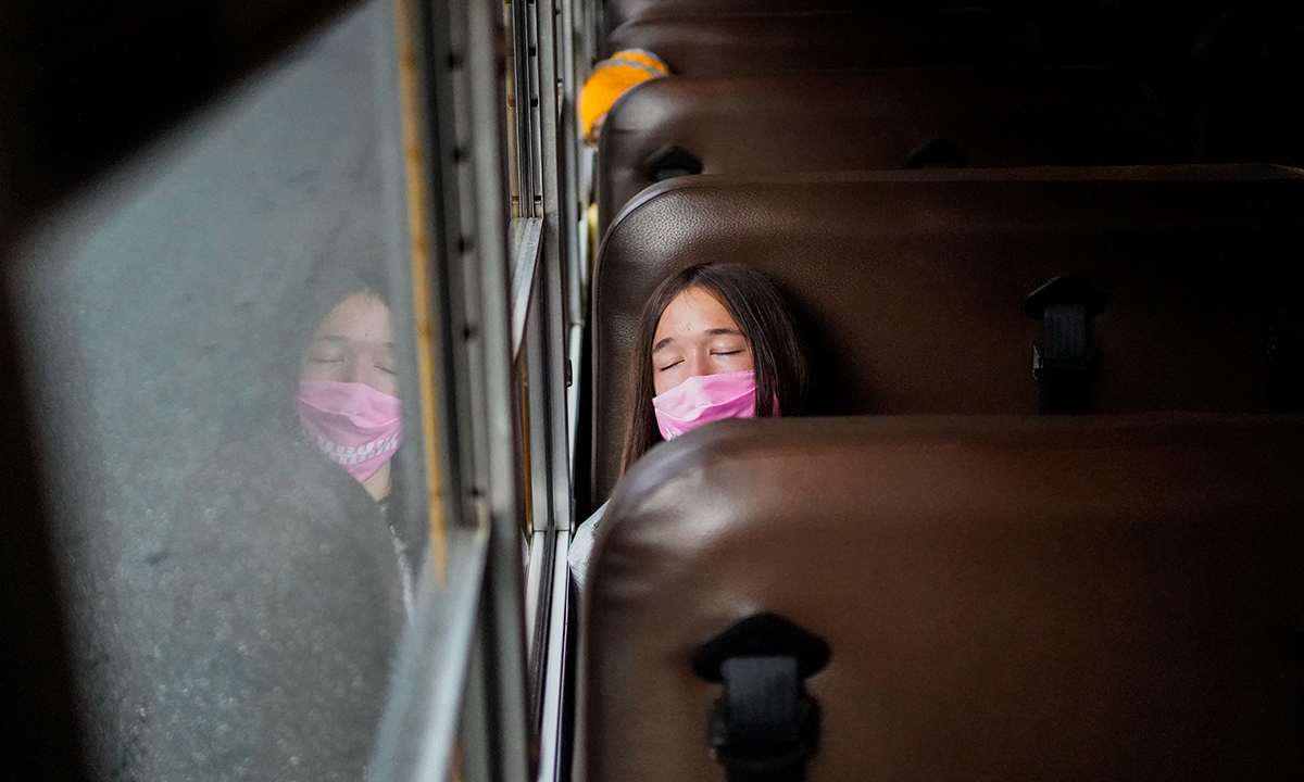 A female student wearing a pink mask sleeps on a school bus.