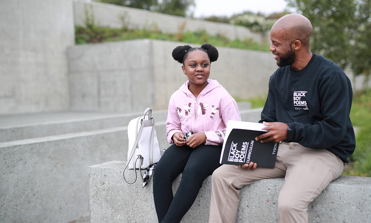 A student sits and talks with Tyson Amir, a poet, outside.