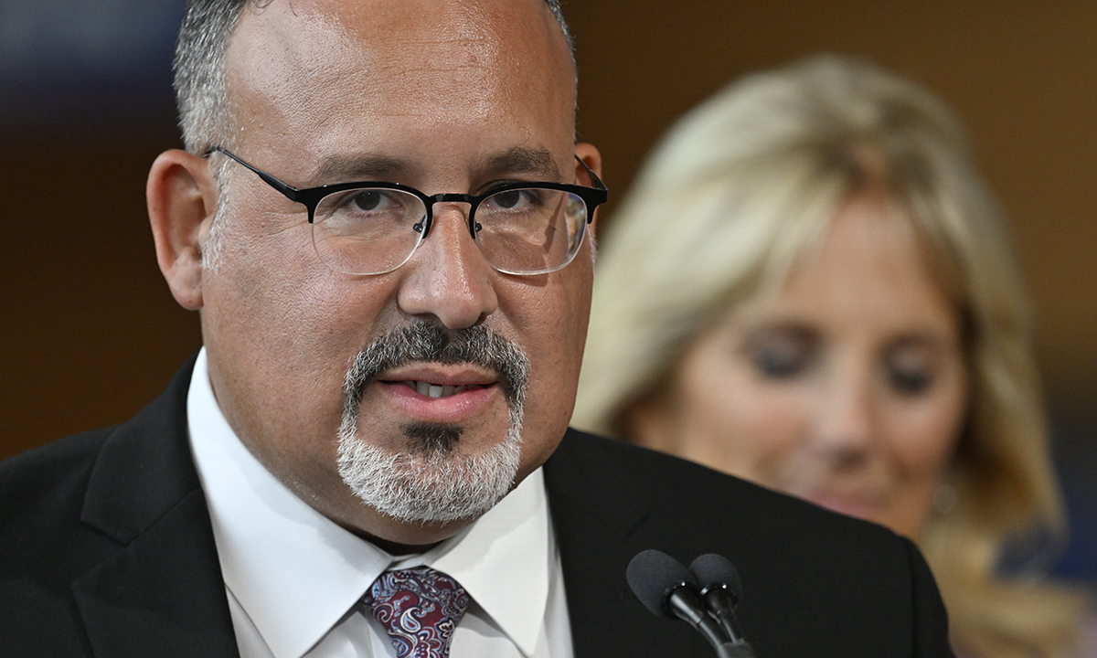 A news photo of Education Secretary Miguel Cardona; First Lady Jill Biden is in the background