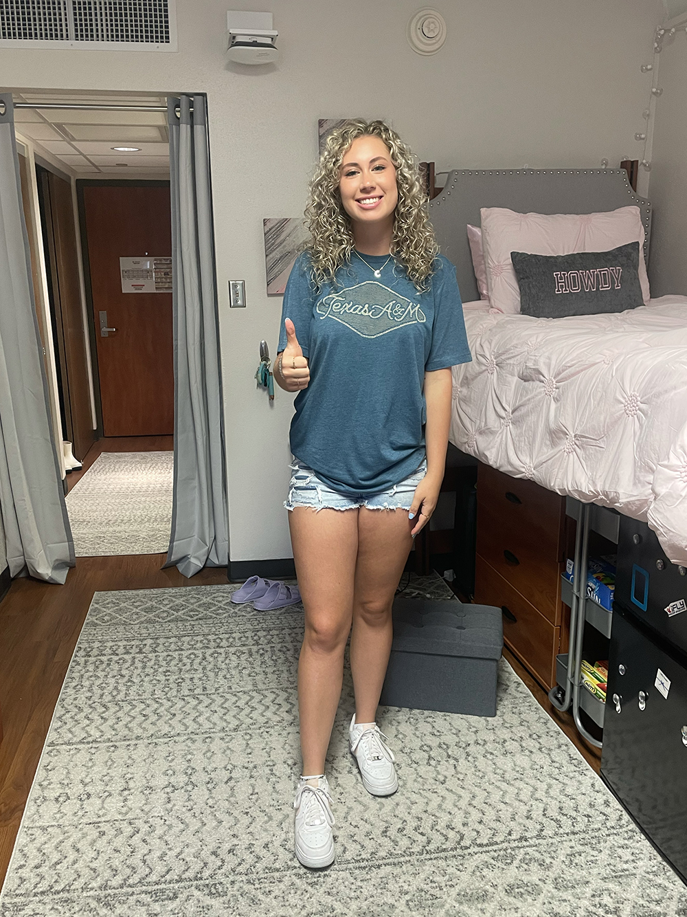 A female student gives a thumbs up while standing in her dorm room