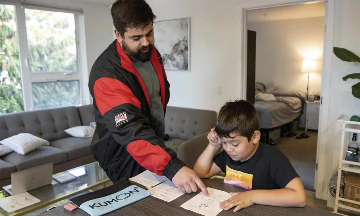 A father is standing, helping his son with homework at a table