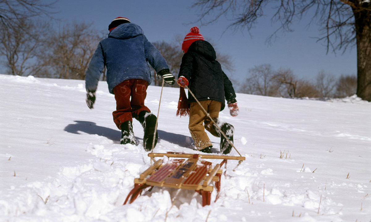A Getty photo two kids running up a snowy hill with a sled
