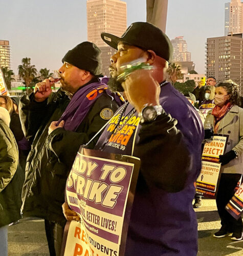 Members of SEIU Local 99 are shown at a rally in LA. One holds a sign that says Ready to Strike; one is blowing a whistle.