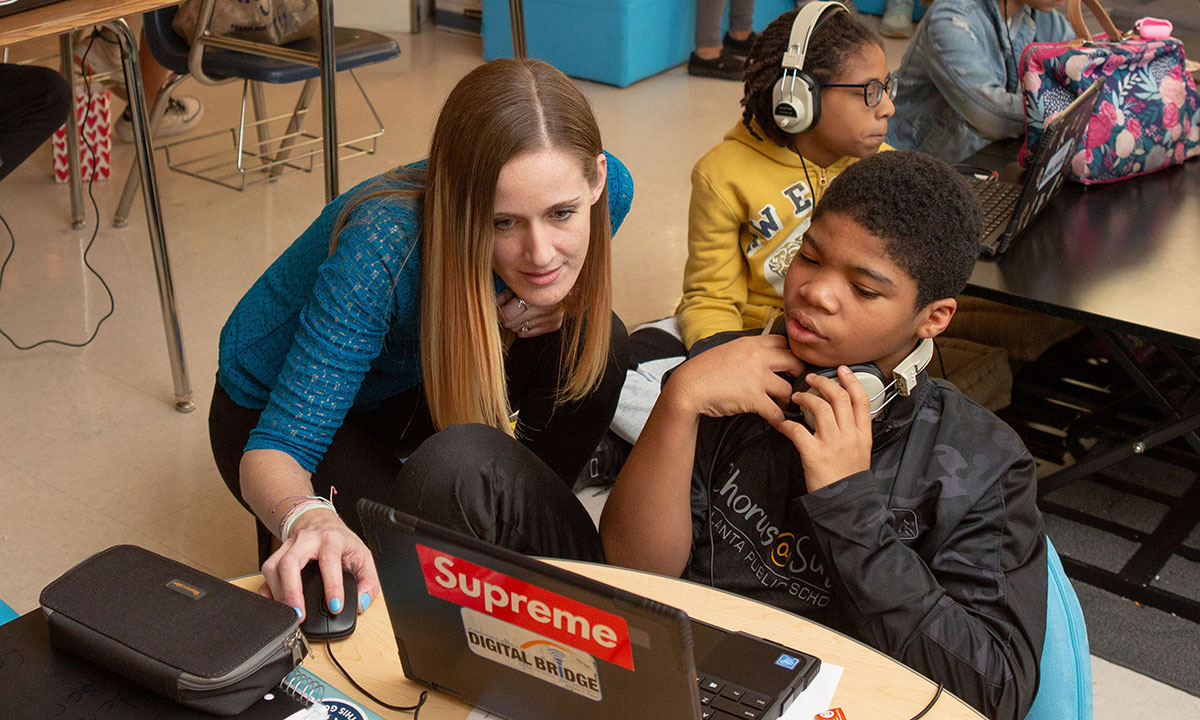 A teacher and student work together on a laptop in a classroom