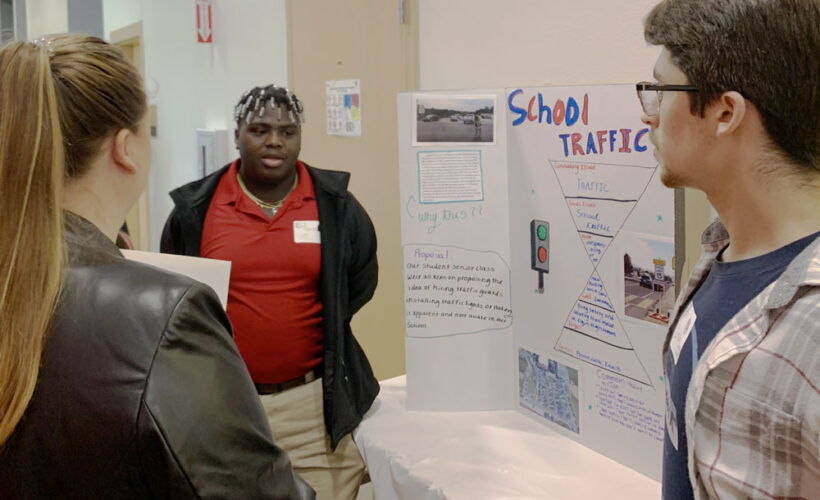 A student stands next to a poster board labeled "School traffic"