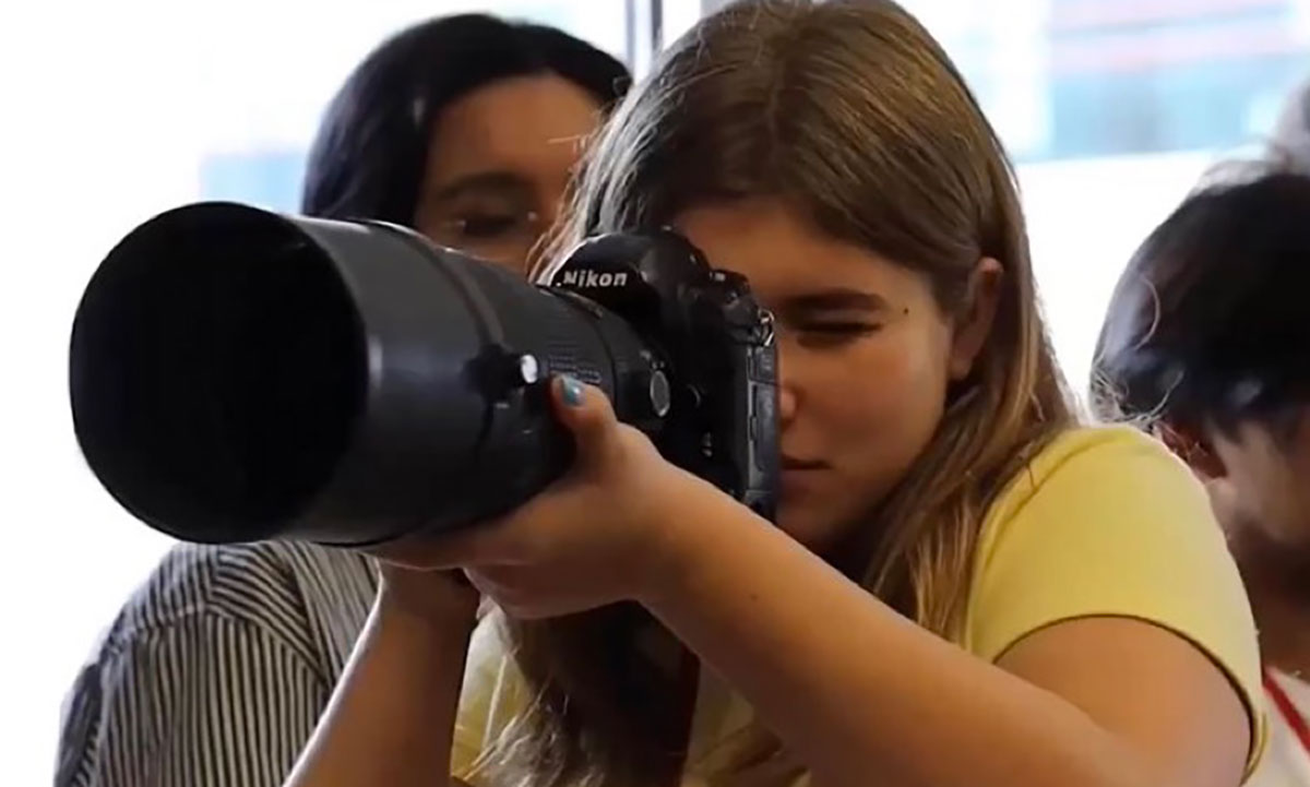 Student journalist Delilah Brumer holds a camera up to her eye to shoot a photo