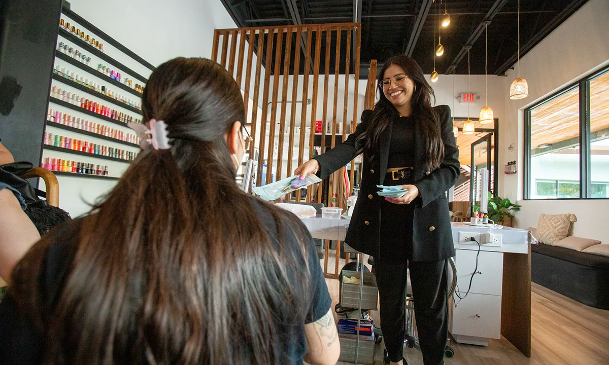 A woman hands manicure implements to one of her employees in a nail salon.