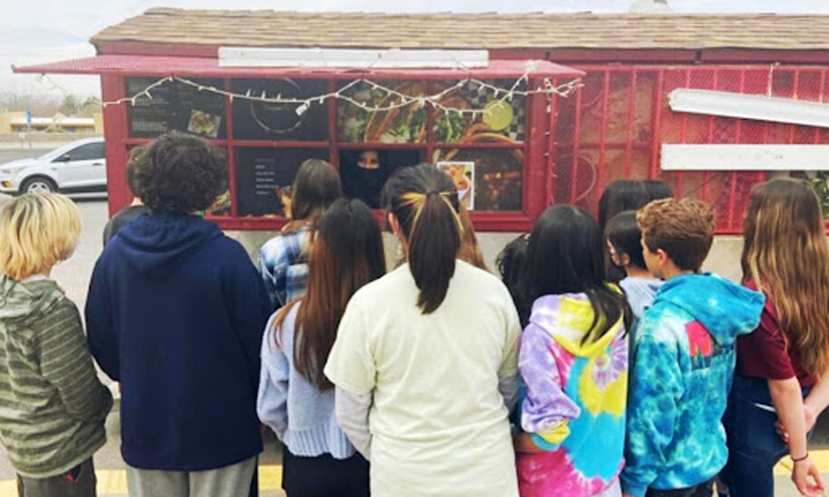 This photo is a group of Sierra Middle School students learning from birria taco truck owner Liz Corrales what it takes to create and maintain a food truck business.