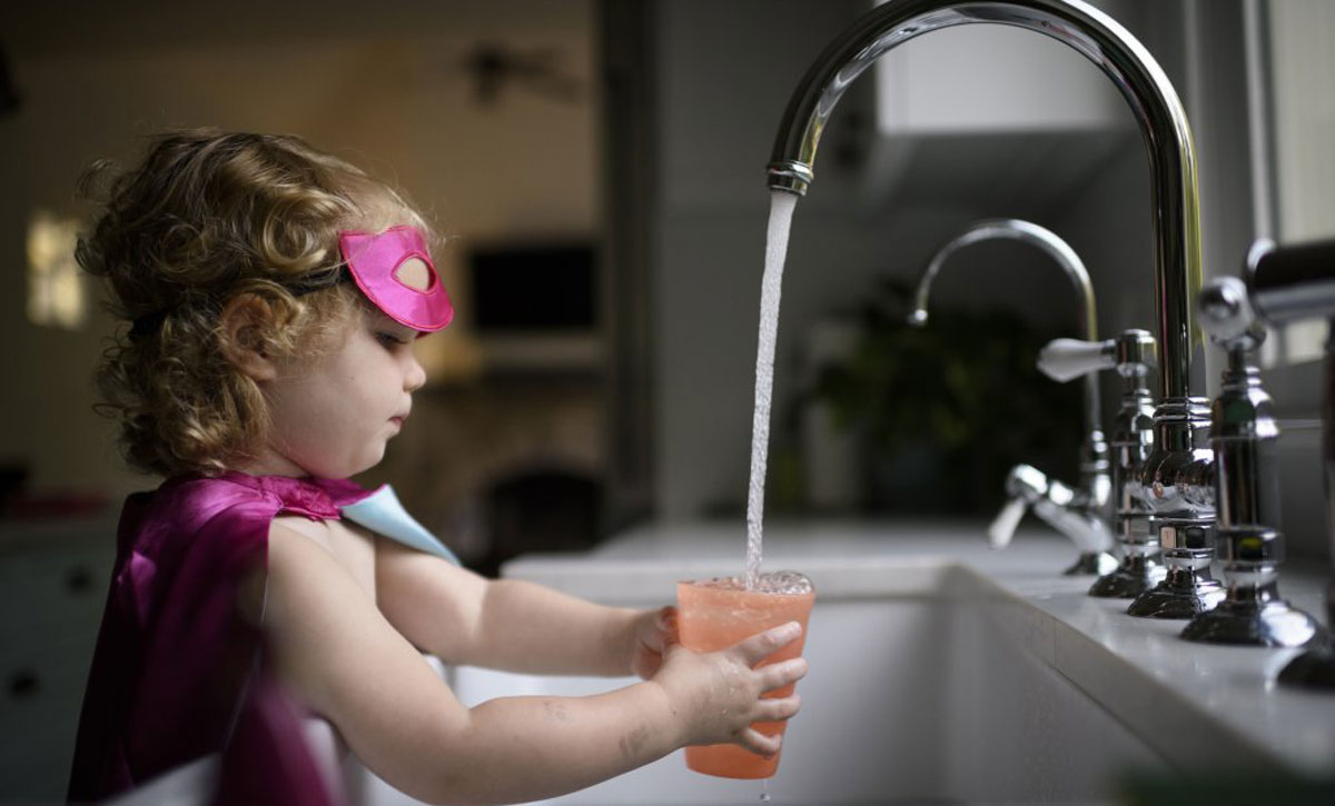 This photo shows a little girl filling up a cup with water at the kitchen sink.