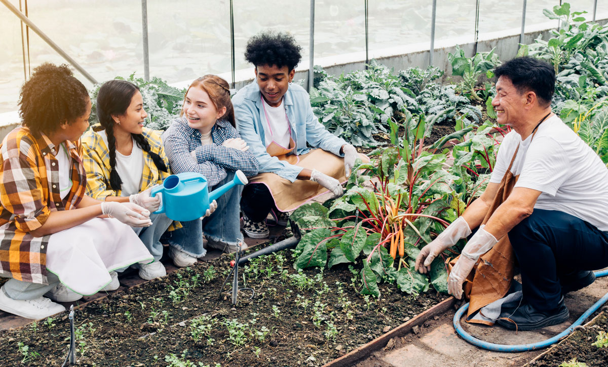 This photo shows four children gardening with an adult outdoors.