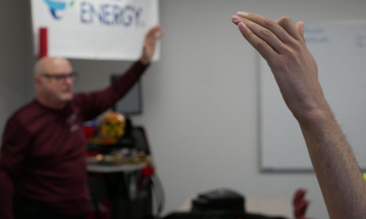 This photo shows a student and teacher raising their hand in class.