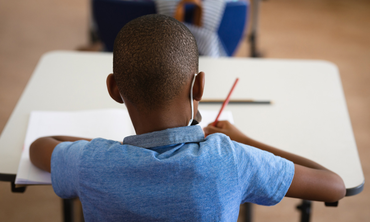 A photo of the rear view of Black student working at their school desk