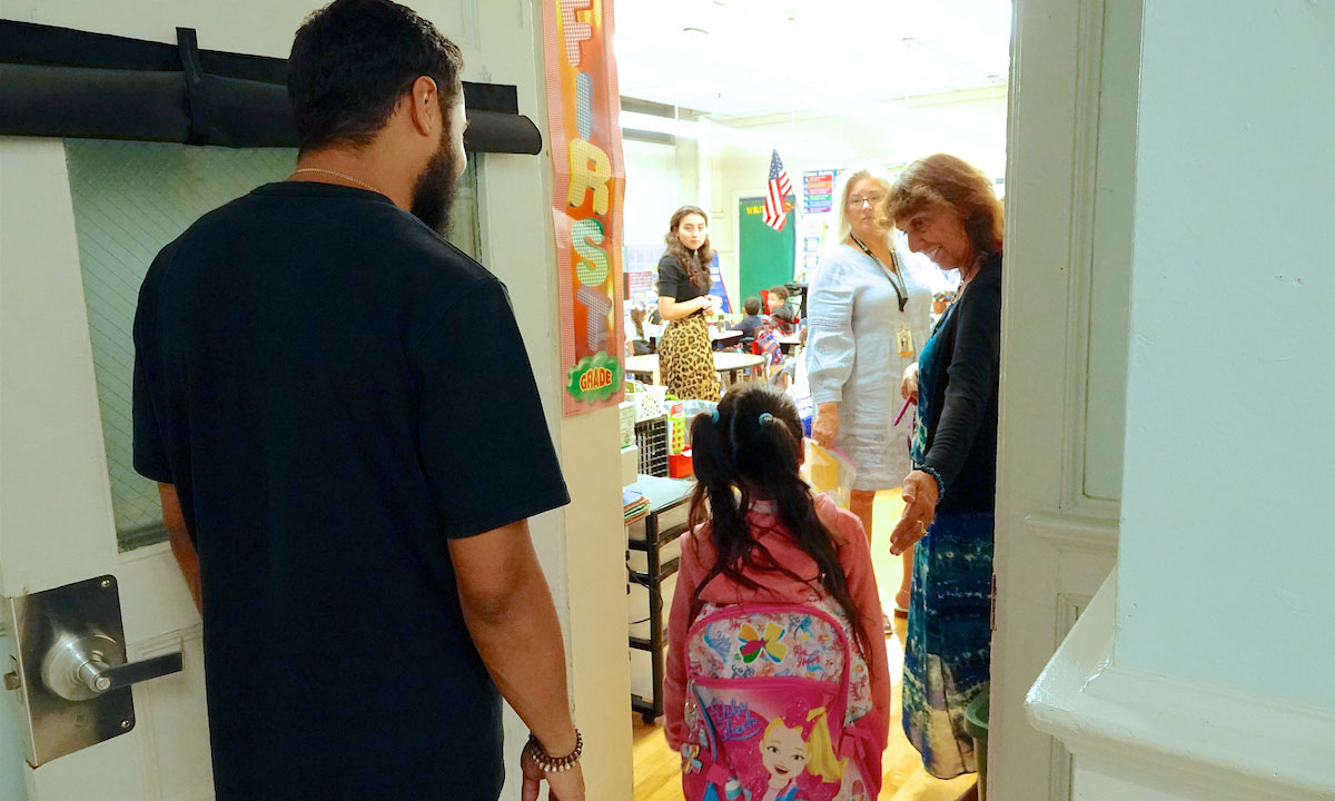This photo shows an little girl entering her classroom with her father.