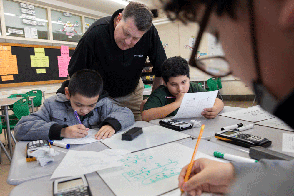 A teacher tutors a small group of students in math in a classroom. 