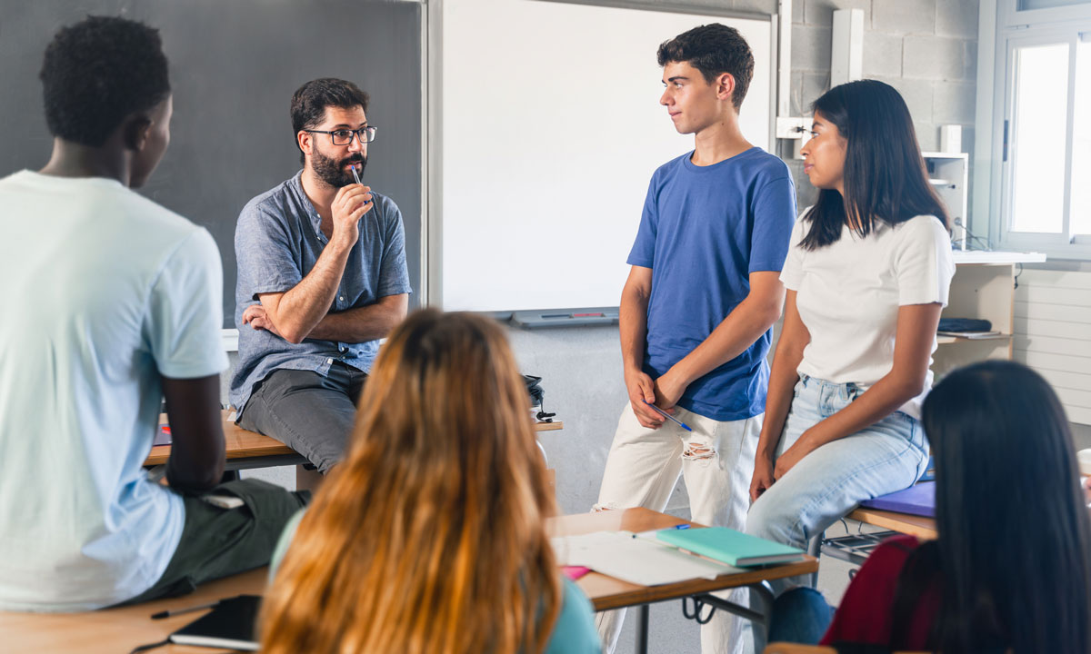 This is a photo of a teacher talking to a small group of students in a circle.