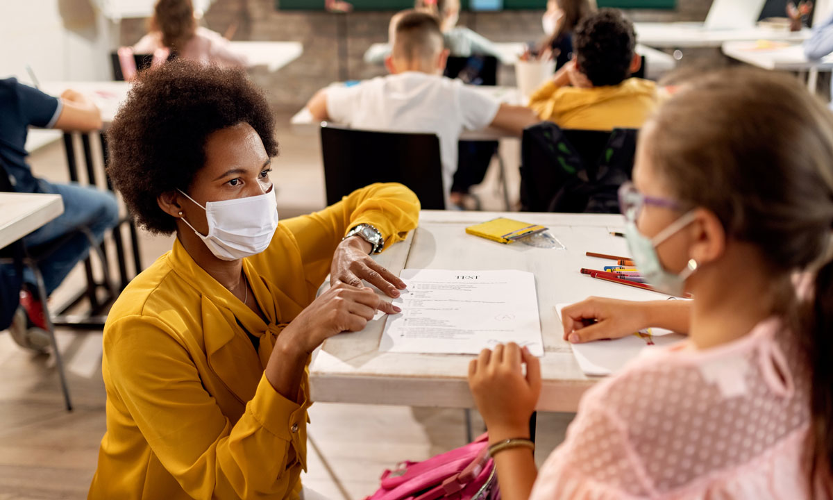 This is a photo of a teacher and student with masks on.