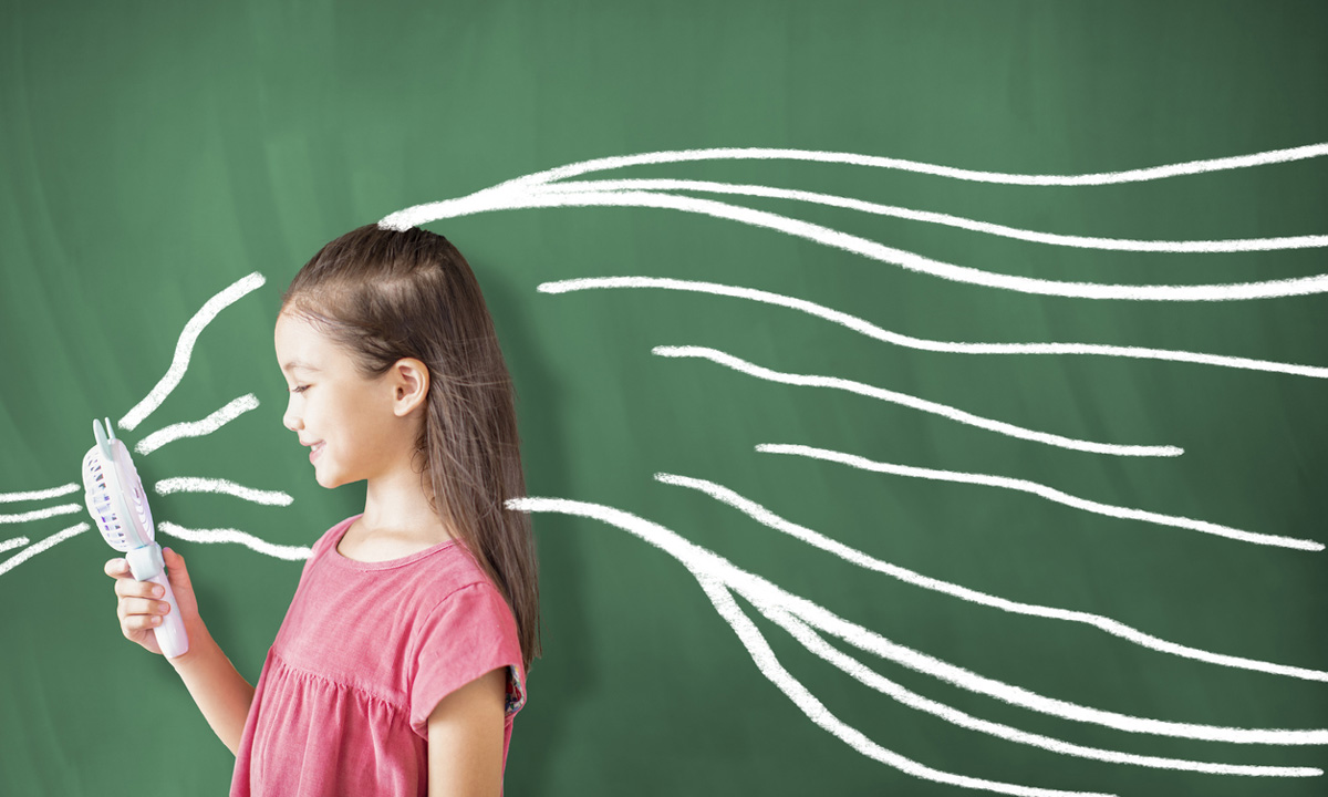 a stock photo of a student holding a personal fan in front of a chalkboard
