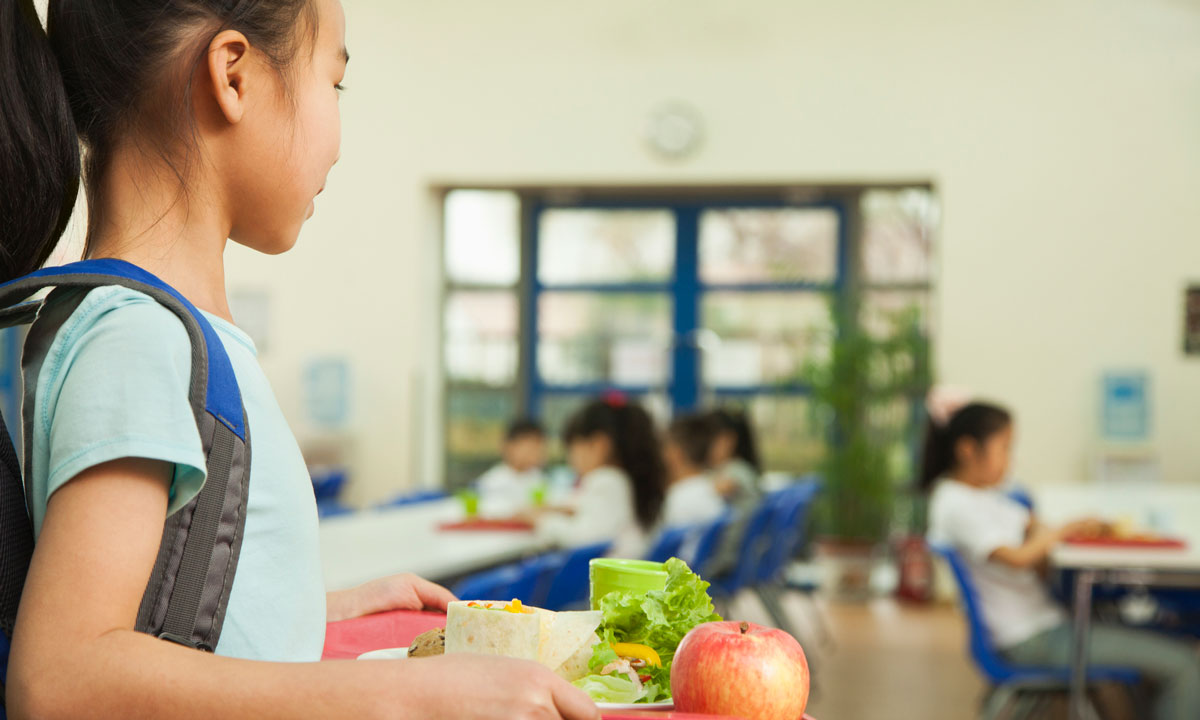 This is a photo of a girl carrying a lunch tray in a school cafeteria.