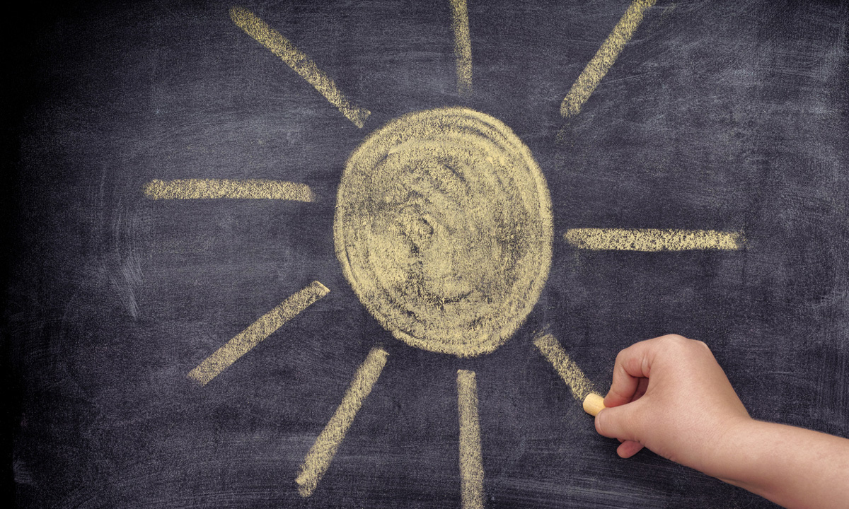 This is a photo of a student drawing a yellow sun on a chalkboard