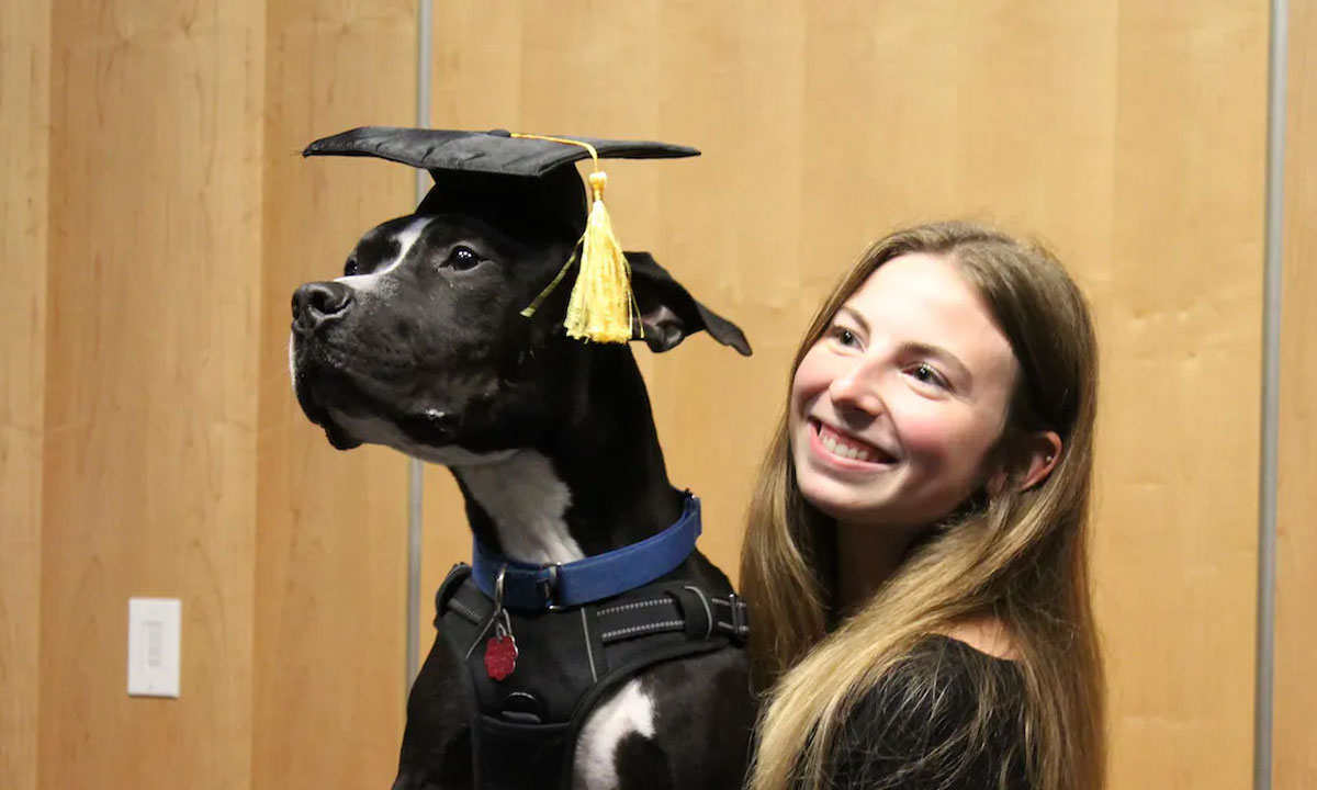 This is a photo of a woman with a dog wearing a graduation cap.