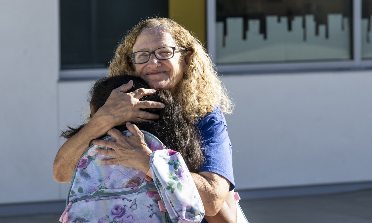A news photo of a teacher welcoming back a student with a hug