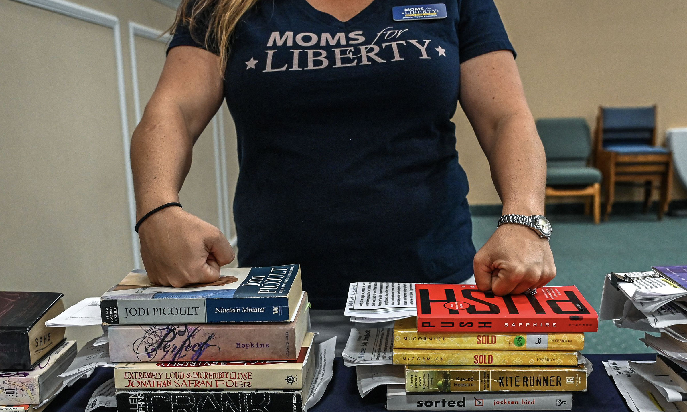 This is a photo of a Moms for Liberty member standing in front of a stack of books.