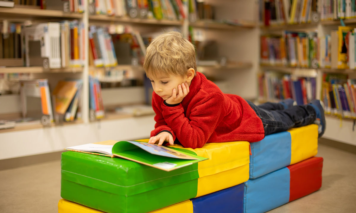 This is a photo of a young boy reading a book in a library.