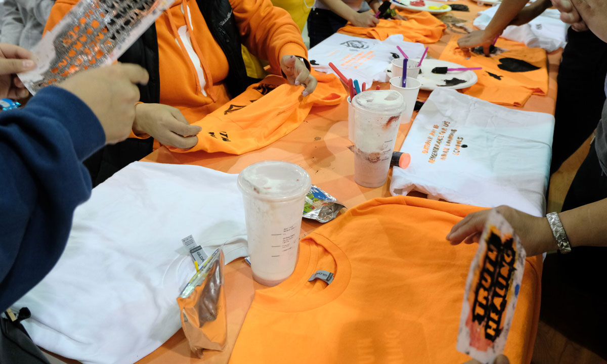 This is a photo of families stenciling orange t-shirts with the message “Truth Healing” at Alaska Native Cultural Charter School in Anchorage.