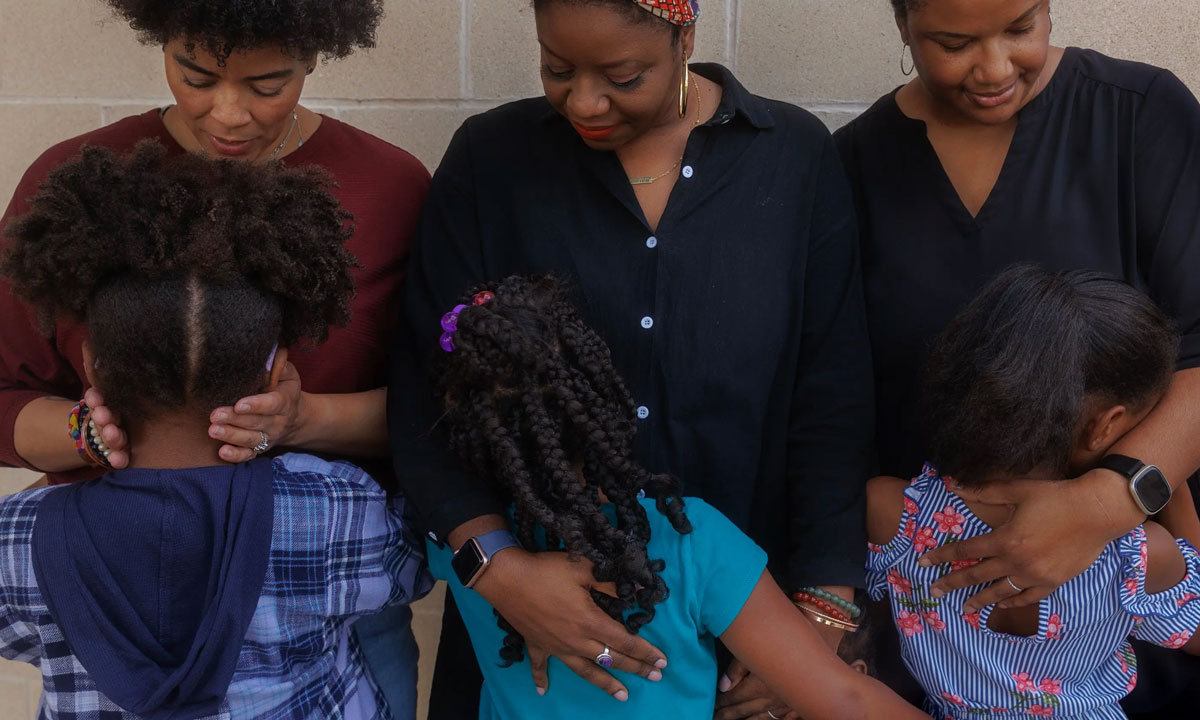 This is a photo of three Black moms hugging their children.