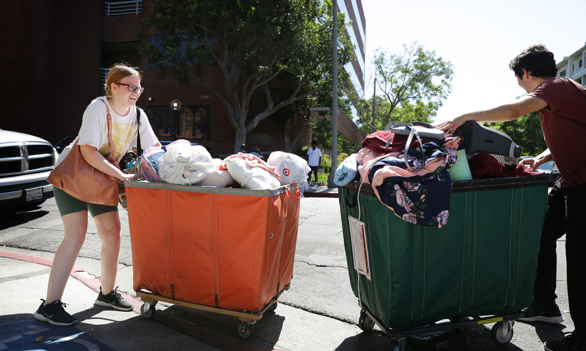 This is a photo of two college students moving into their dorms with carts outside.