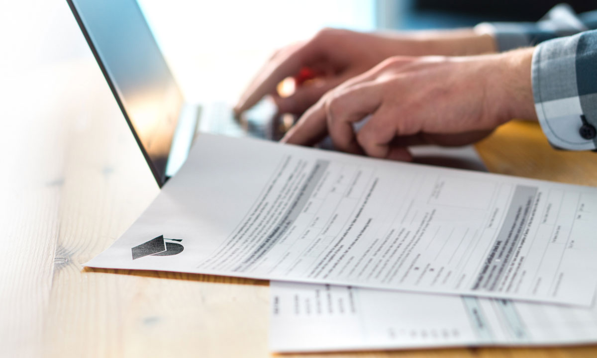 This is a photo of a person typing on a laptop with graduation paperwork on the desk.