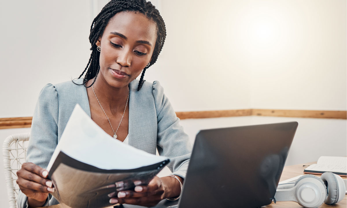 This is a photo of a woman filling out paperwork with a laptop.