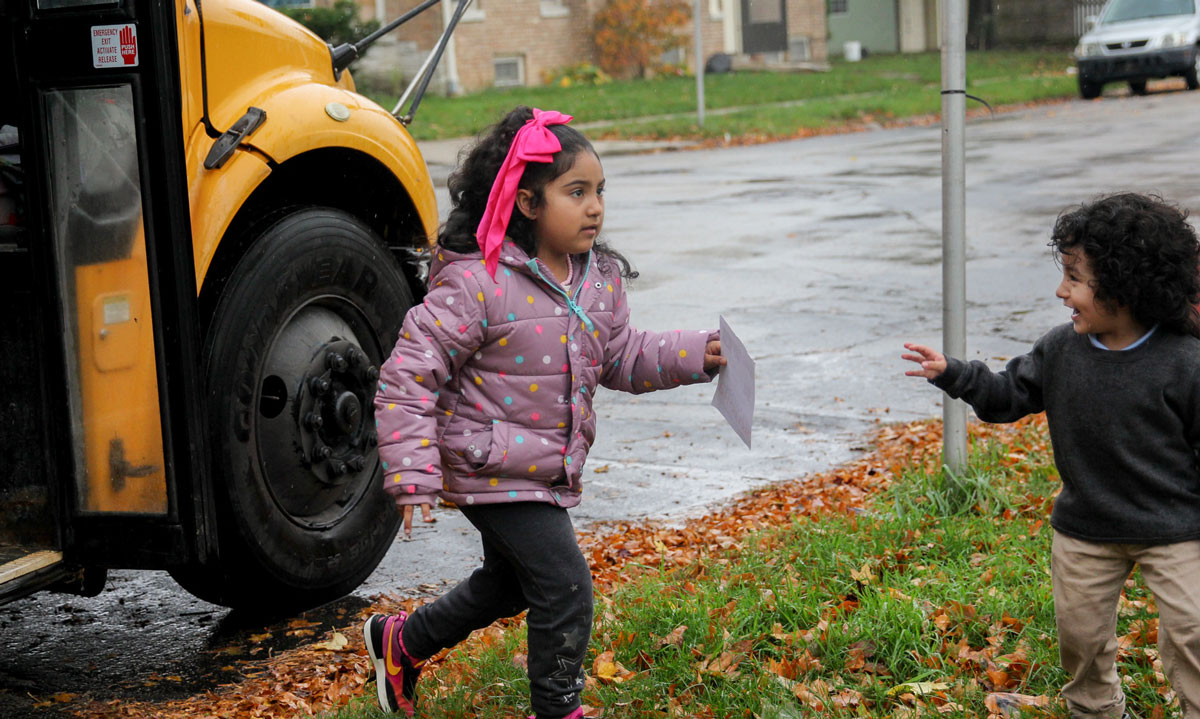 This is a photo of a young girl being greeted by her little brother off of the school bus.