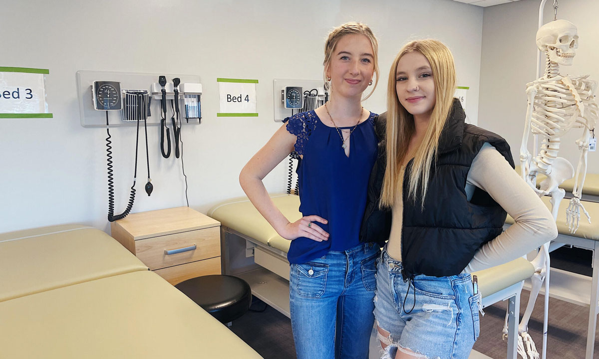 This is a photo of two teenage girls pursuing careers in nursing posing in a mock doctor's office at a charter school.
