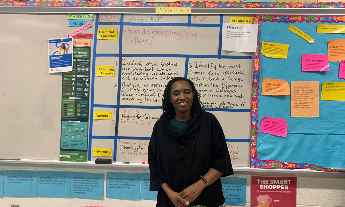 This is a photo of Ms. Ogede standing in front of her class board.