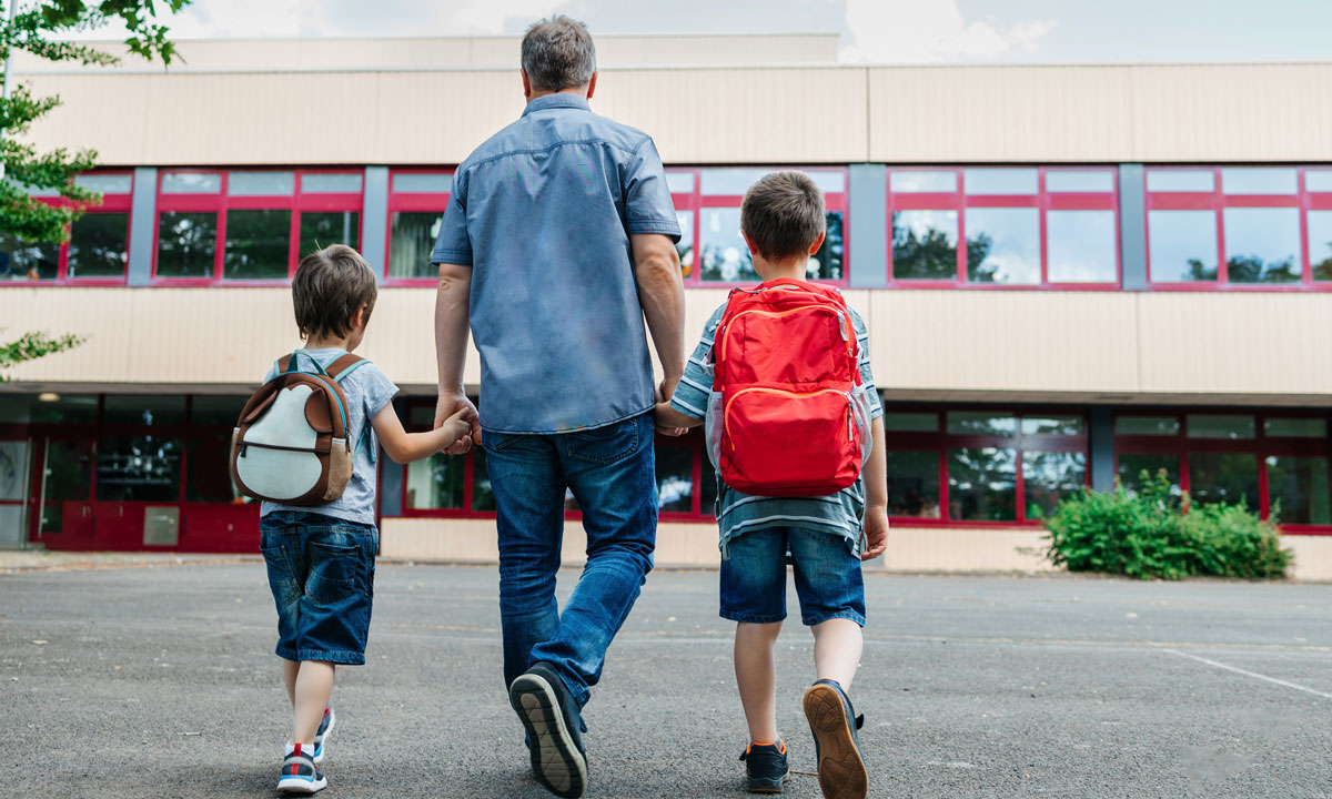 This is a photo of a dad walking his two sons into school.