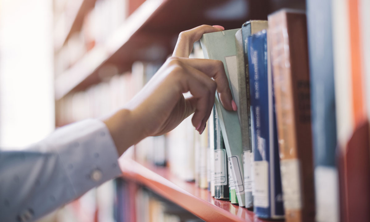 This is a photo of someone picking a book from a library shelf.