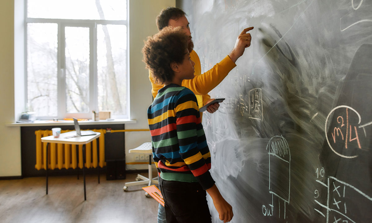 This is a photo of a student and teacher a ta chalkboard doing math.