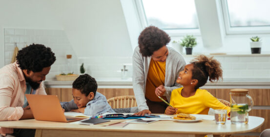 This is photo of an African American mom and dad homeschooling their son and daughter.
