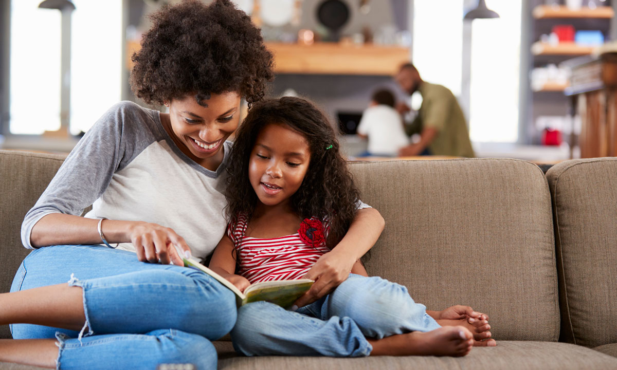 This is a photo of a young girl and her mom reading on the couch.
