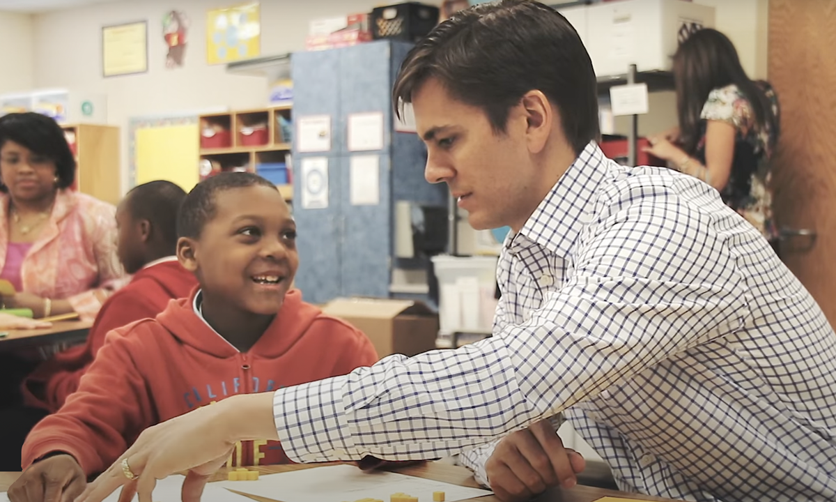 This is a photo of a tutor working with a third grader at his desk.