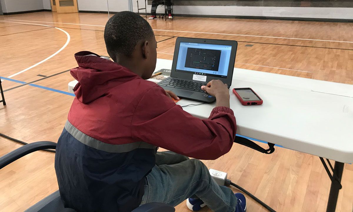 This is a photo of a student working on a laptop in a school gymnasium.